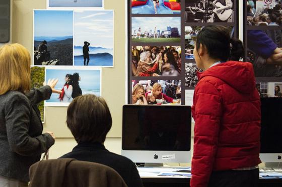 Photo of a group of women consulting a wall of printed photographs above a designer's desk. 