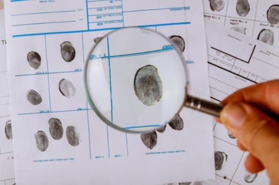 Photo of a hand holding a magnifying glass over fingerprints